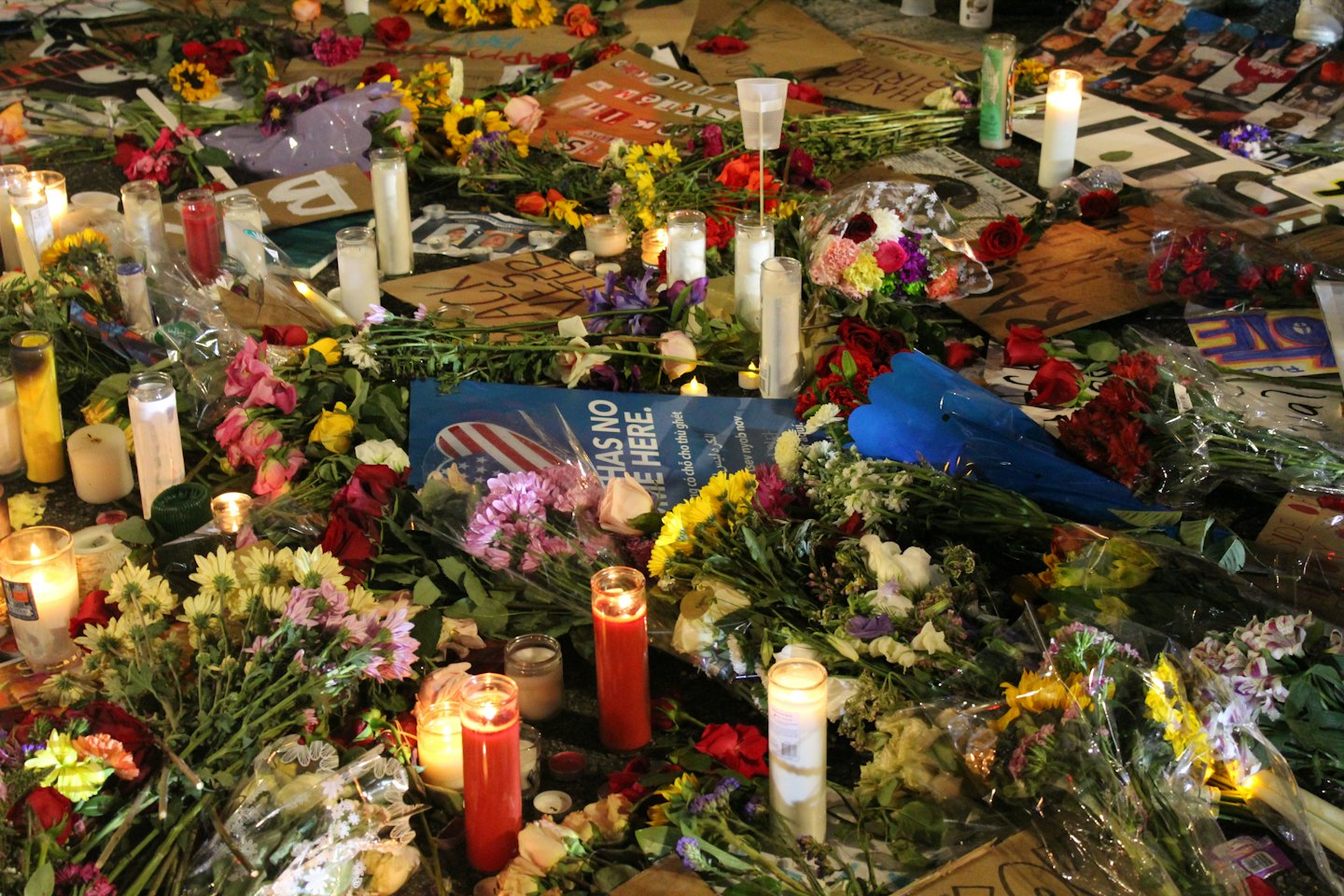 Lit candles and floral bouquets at a street memorial.