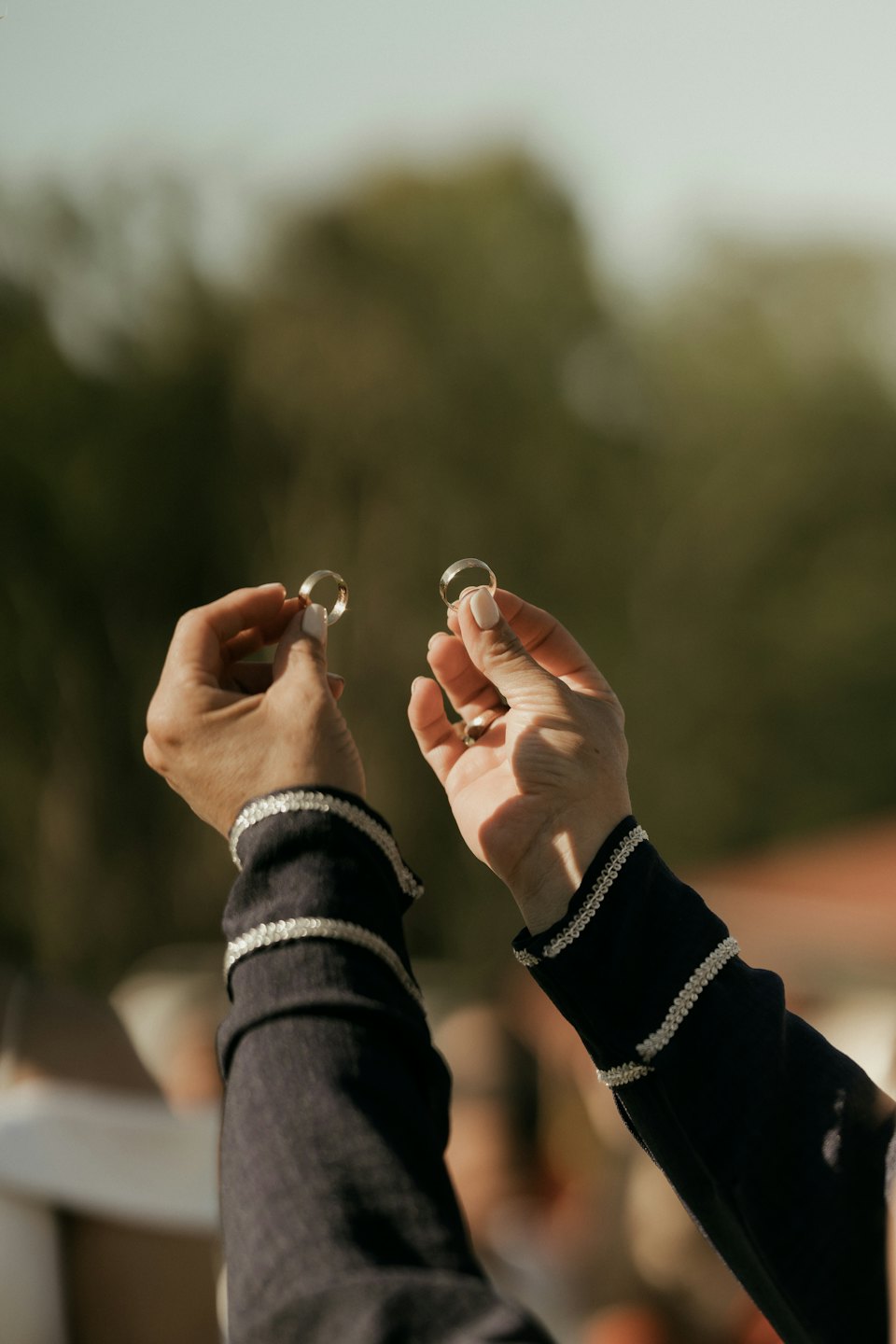 Two hands hold up golden wedding rings outdoors.