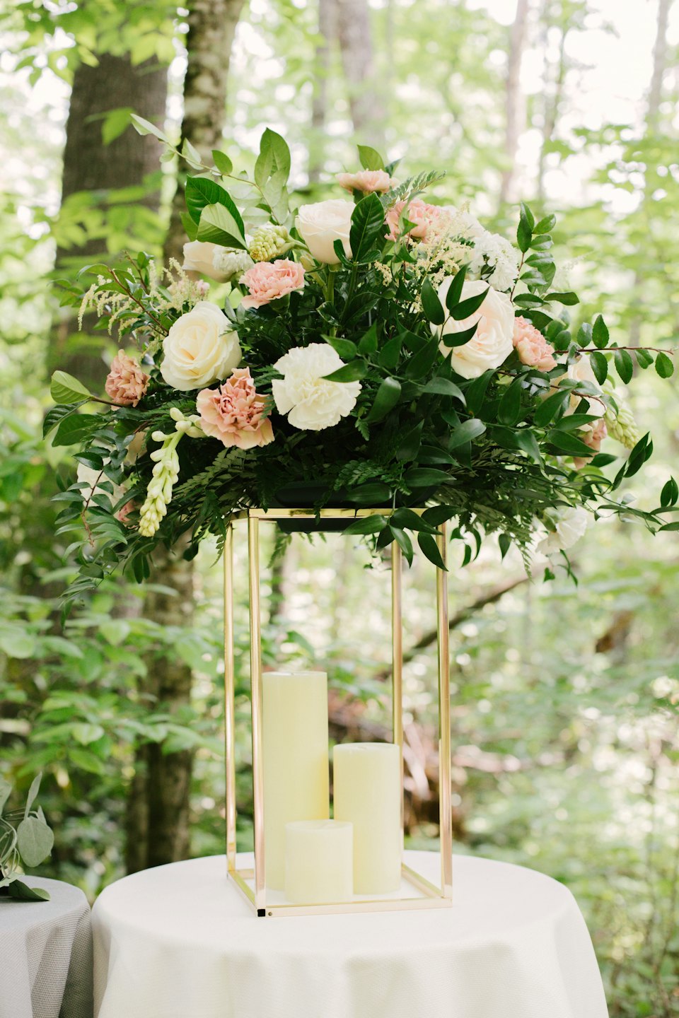 Floral centerpiece with white roses and candles on a forest table.