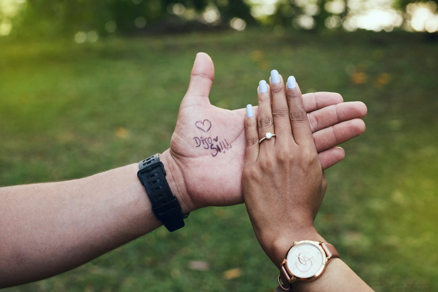 Two hands joined together showing an engagement ring and written message.