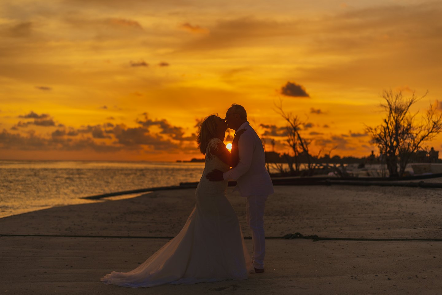 Couple silhouetted kissing at sunset beach ceremony.