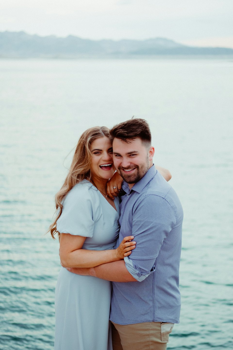 A couple embraces while standing in front of a lake.