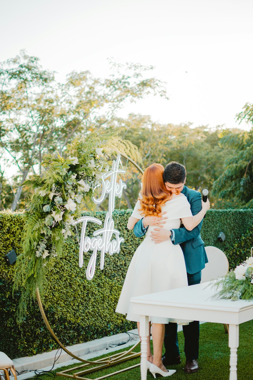 Couple embraces at outdoor ceremony with 'Better Together' sign.