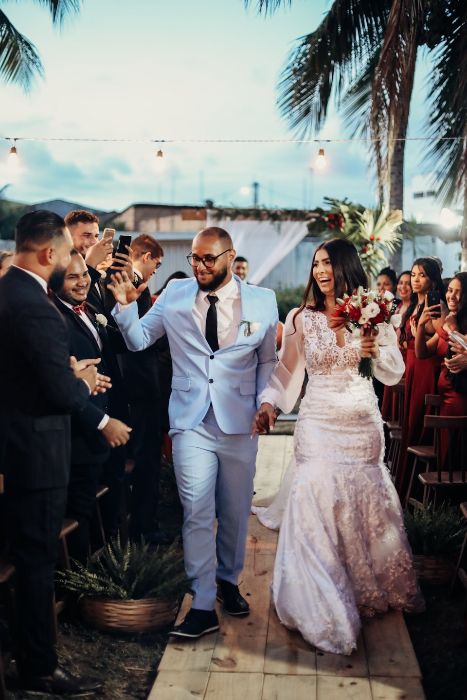 Couple holding hands walking down outdoor aisle at sunset.