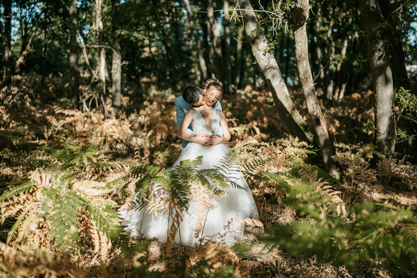 Newlywed couple embracing while standing among ferns in a forest.