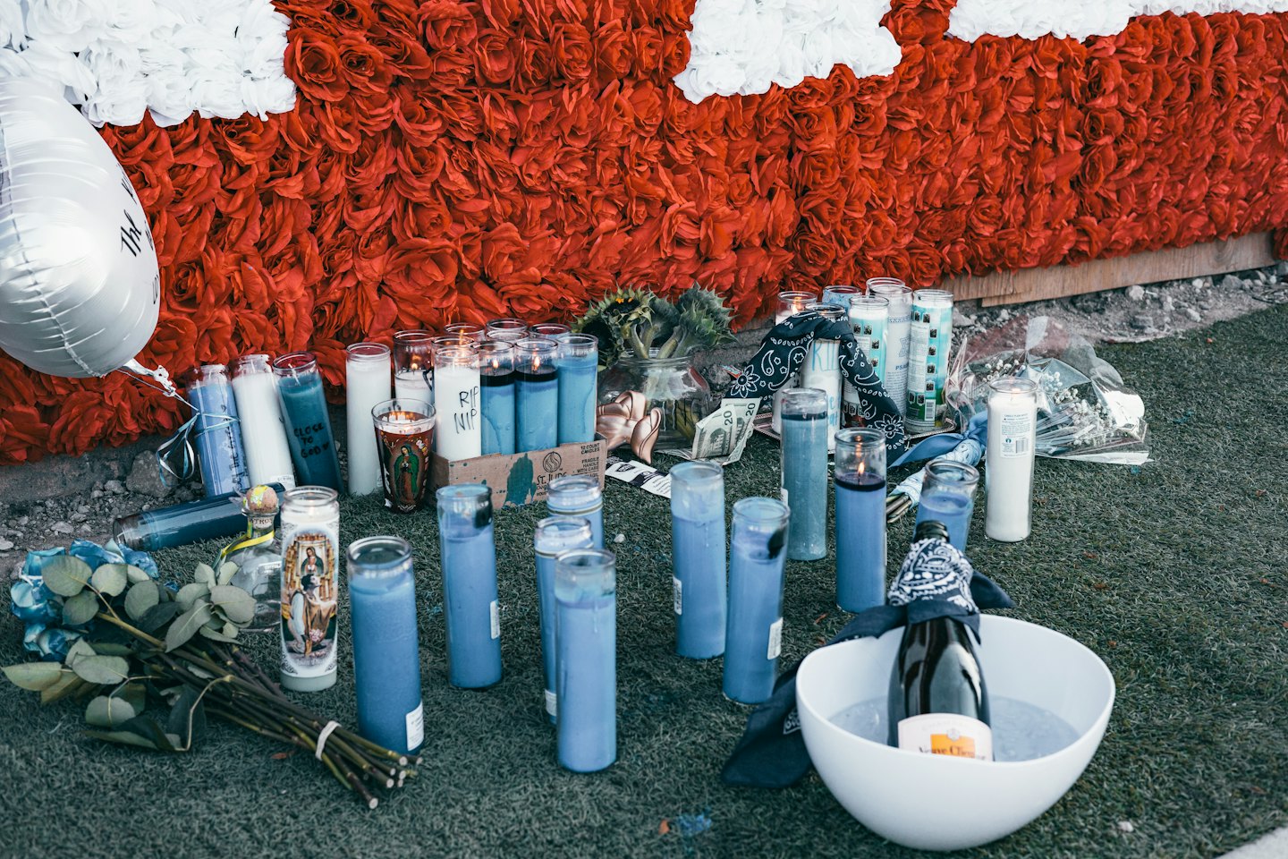 Lit memorial candles and flowers placed against a floral wall.