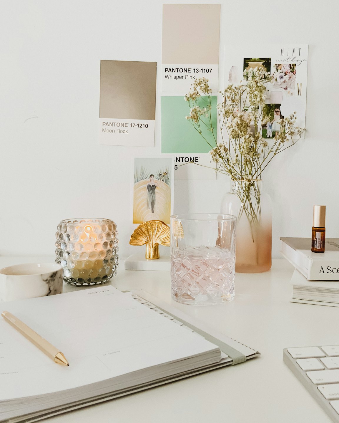 Desk with planner, candle, and flowers next to inspiration boards.