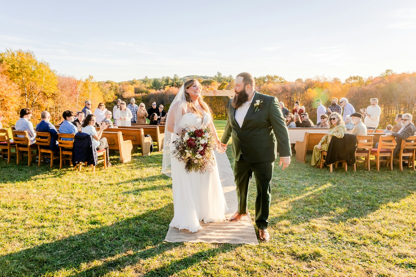Newlyweds walking hand in hand through an autumn wedding ceremony.