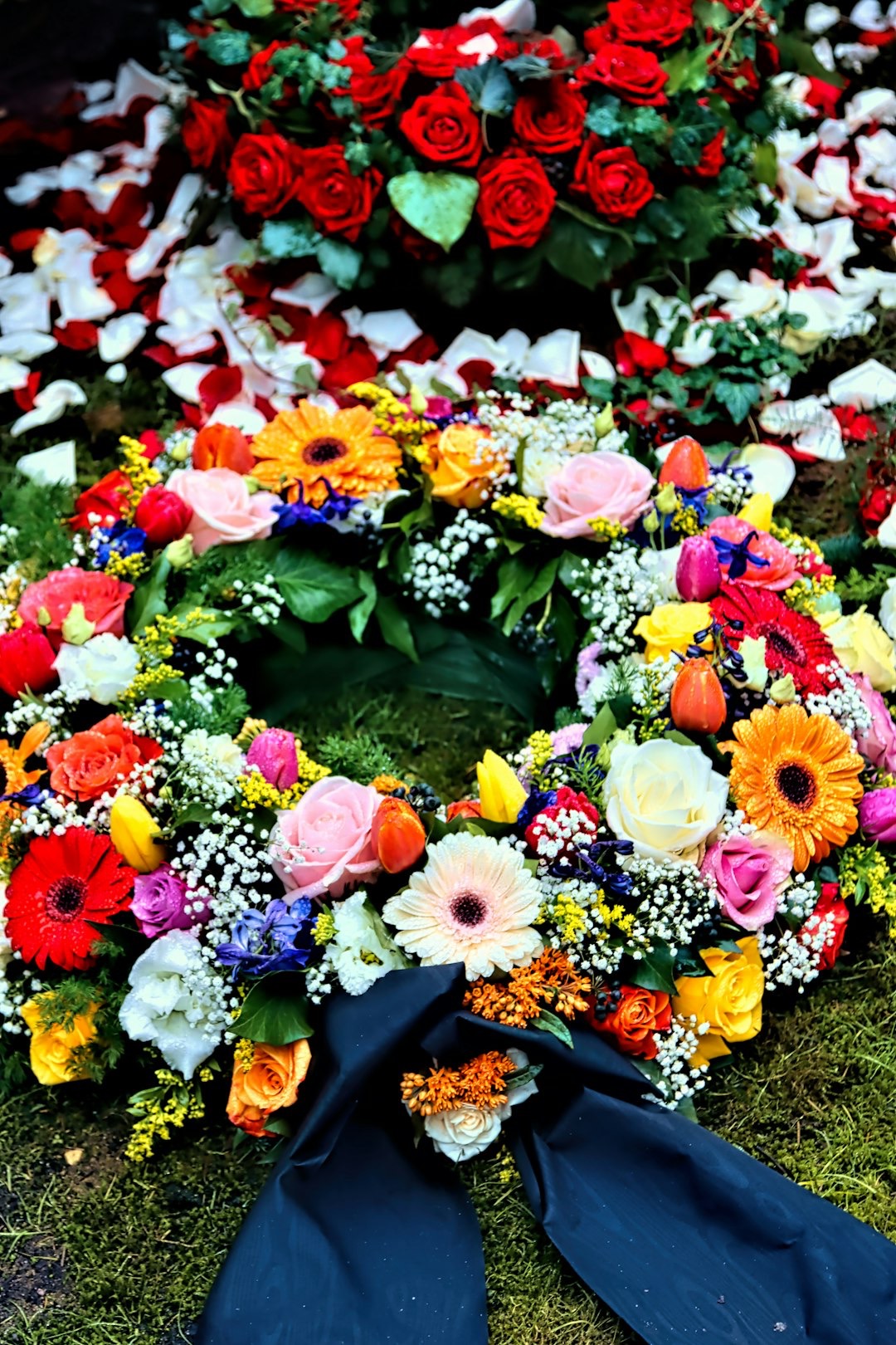 A floral wreath with colorful roses and tulips rests on grass.