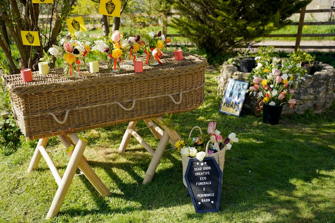 A wicker coffin decorated with flowers sits in a grassy field.